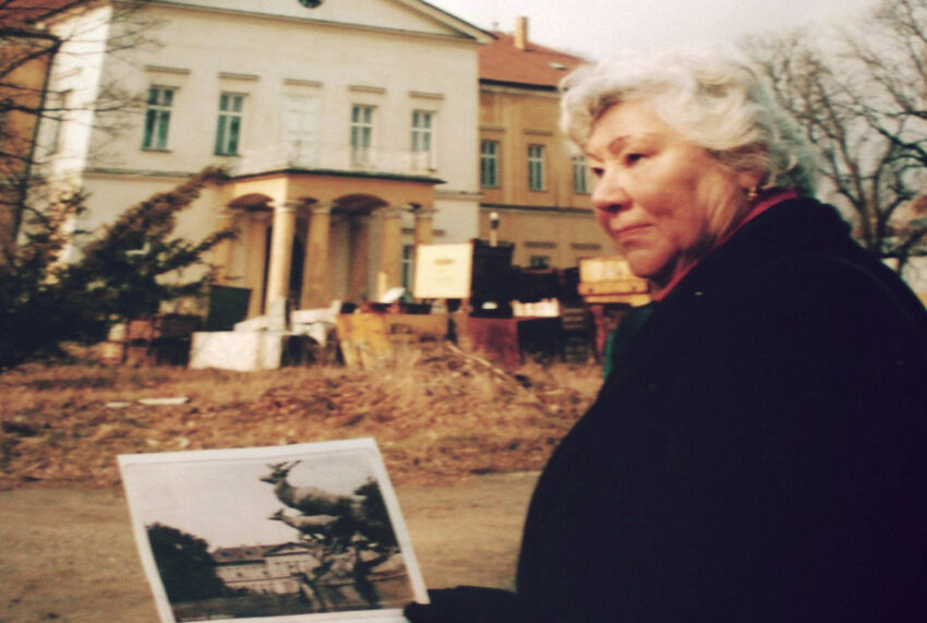 Helena Vovsová u dolního zámku v Panenských Břežanech s fotografií soch jelenů odstraněné Linou Heydrichovou. Zdroj: Paměť národa